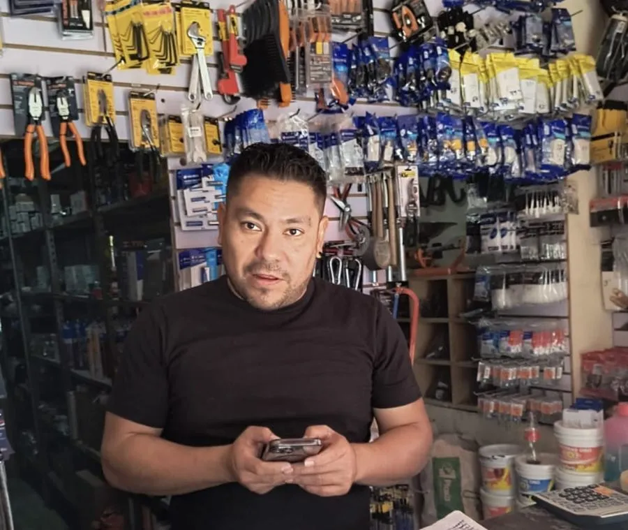 Francisco con su celular en el mostrador, frente a la pared de herramienta